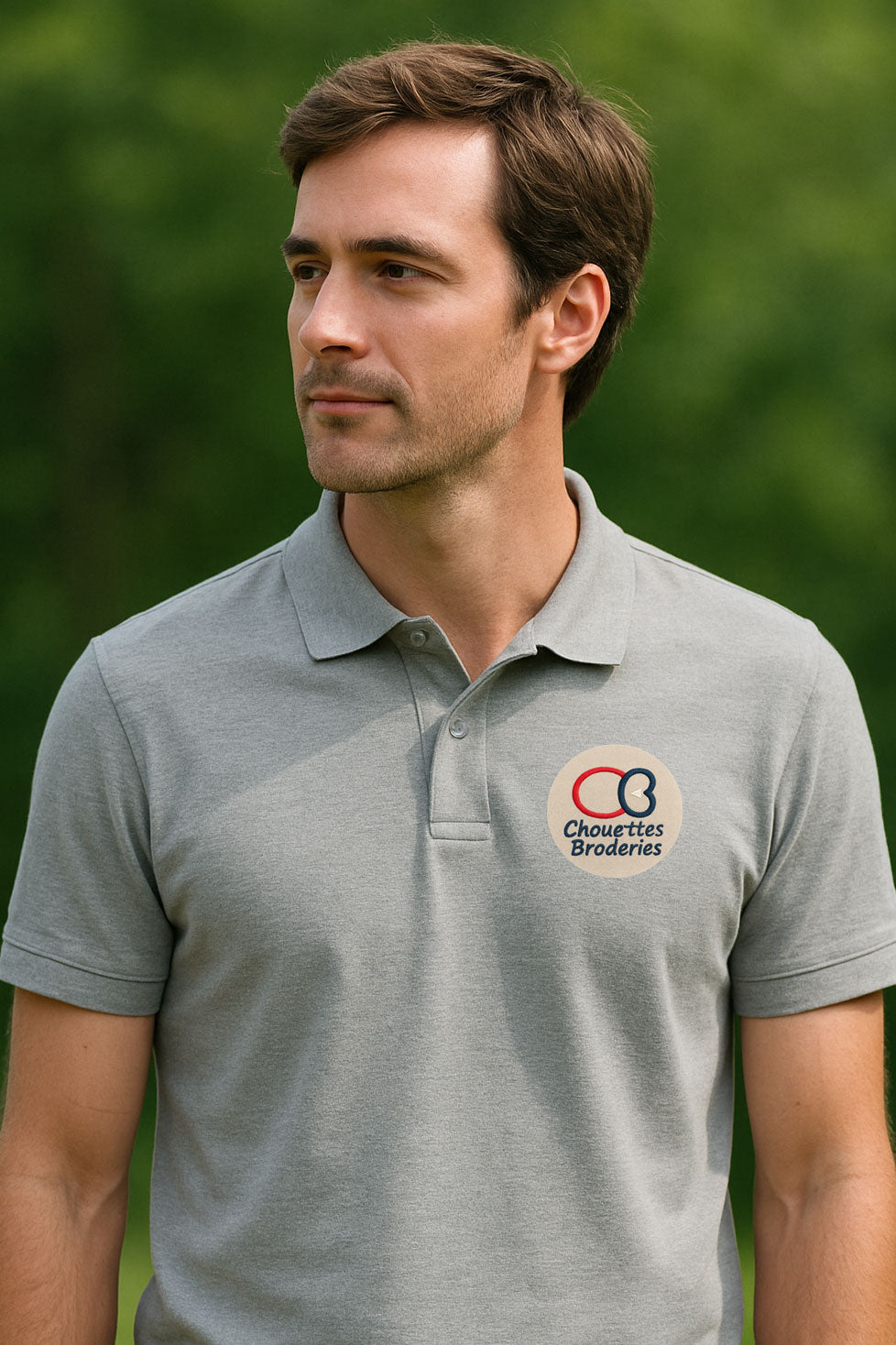 Homme portant un polo gris clair, debout en extérieur, avec fond de verdure flou – image illustrative pour la broderie de logo professionnelle