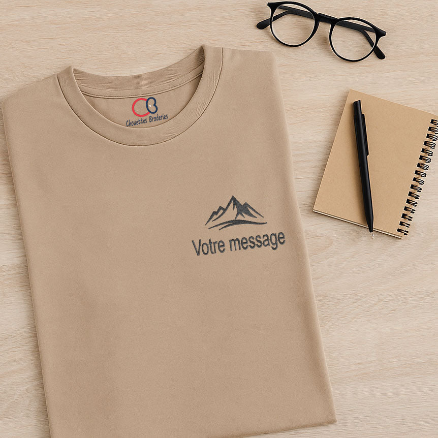 T-shirt homme sable mouillé plié sur table, avec broderie montagne en noir et message personnalisable, idée cadeau originale