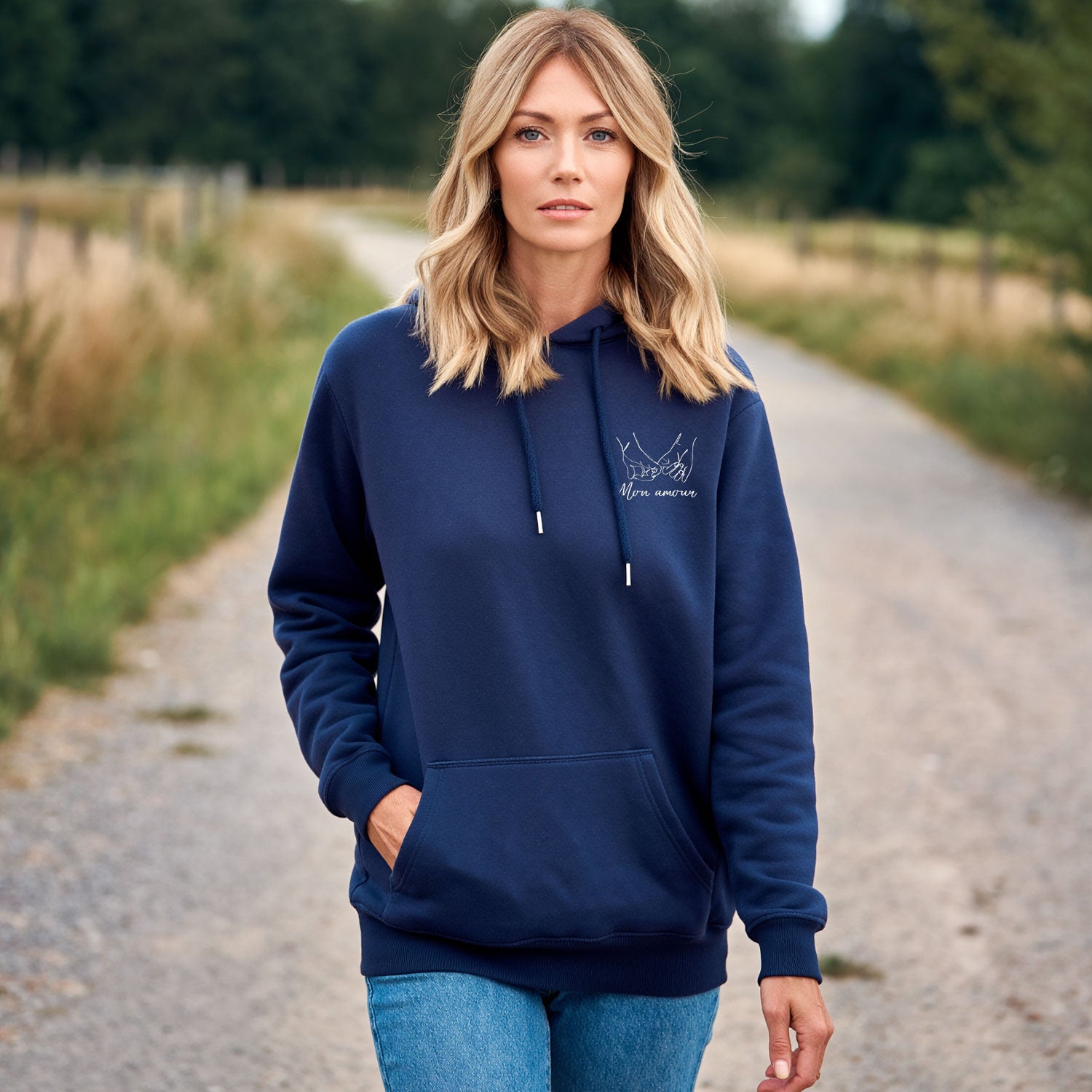 Femme portant un sweat à capuche bleu marine brodé avec motif mains entrelacées, sweat personnalisé pour couple, porté en extérieur dans un cadre naturel