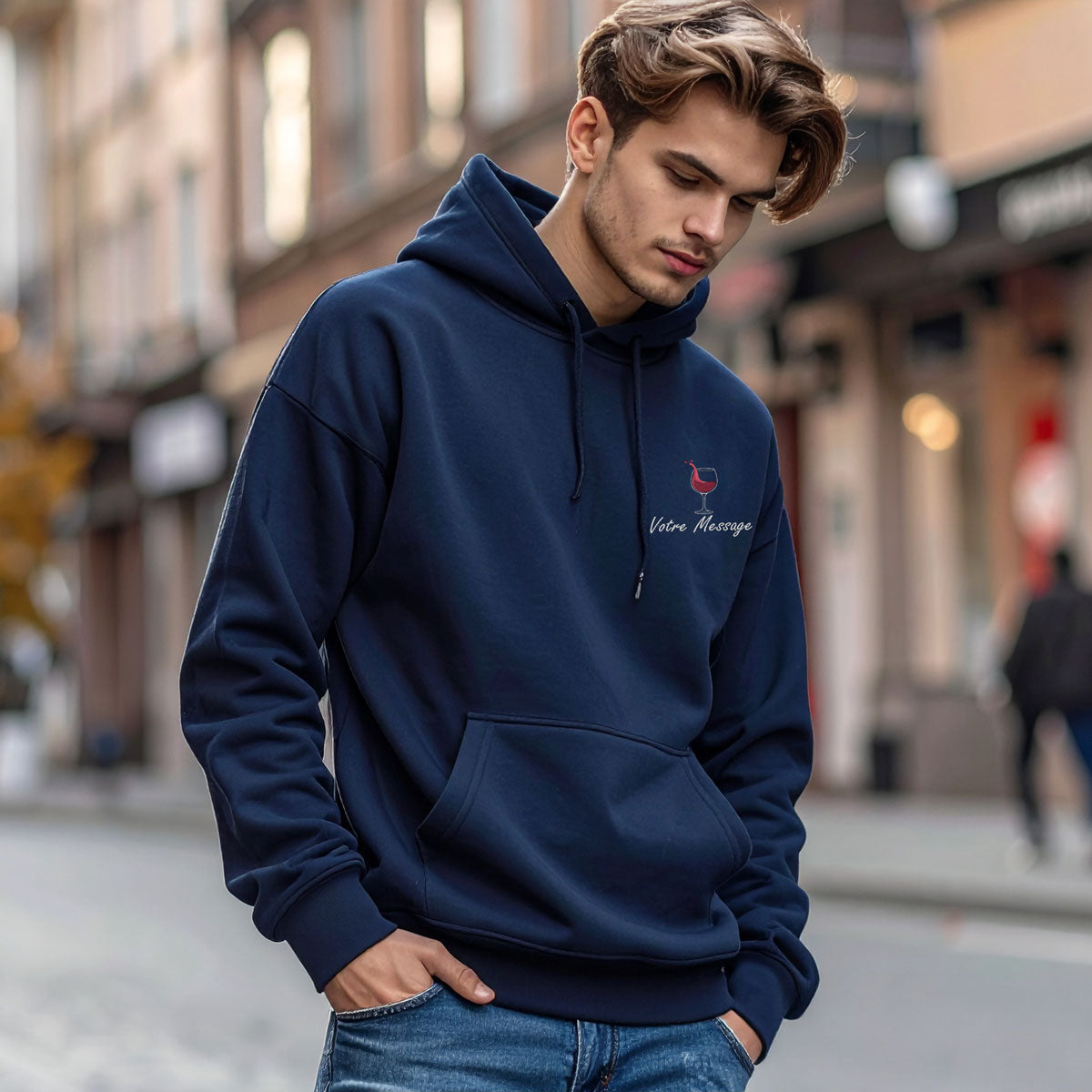 Homme portant un sweat à capuche bleu marine avec broderie personnalisée "Votre message" et un motif de verre de vin, photo en extérieur style urbain.