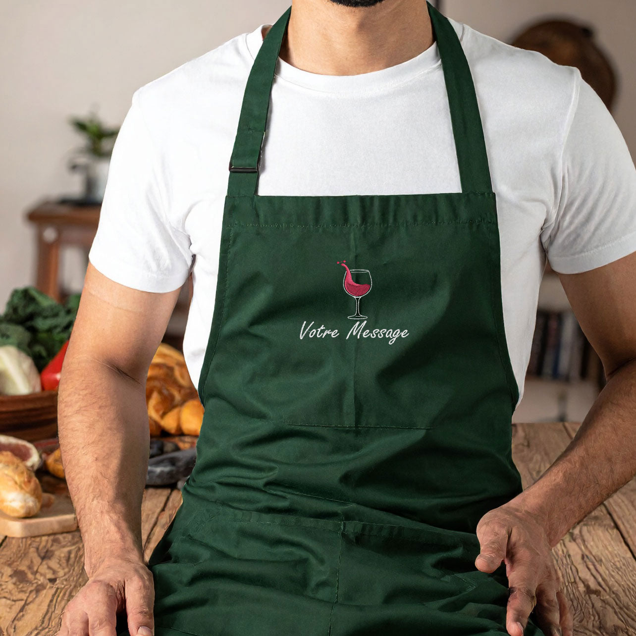 Tablier personnalisé brodé vert bouteille avec motif et texte, porté par un homme en cuisine — idée cadeau originale pour homme ou femme.