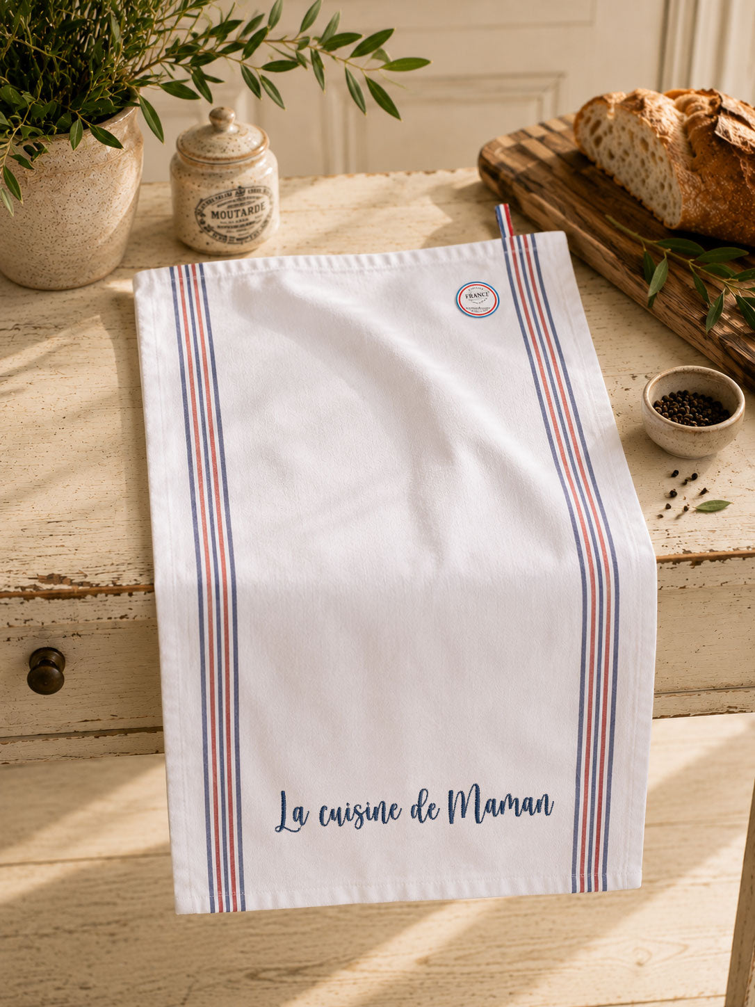 Torchon de cuisine personnalisé brodé « La cuisine de… » en coton, Made in France, présenté dans une cuisine chaleureuse. Idée cadeau personnalisée pour la cuisine.