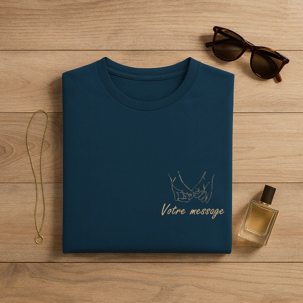 T-shirt bleu petrole plié sur table en bois, idéal pour broderie personnalisée, présenté avec accessoires élégants – une belle idée cadeau unique et minimaliste.