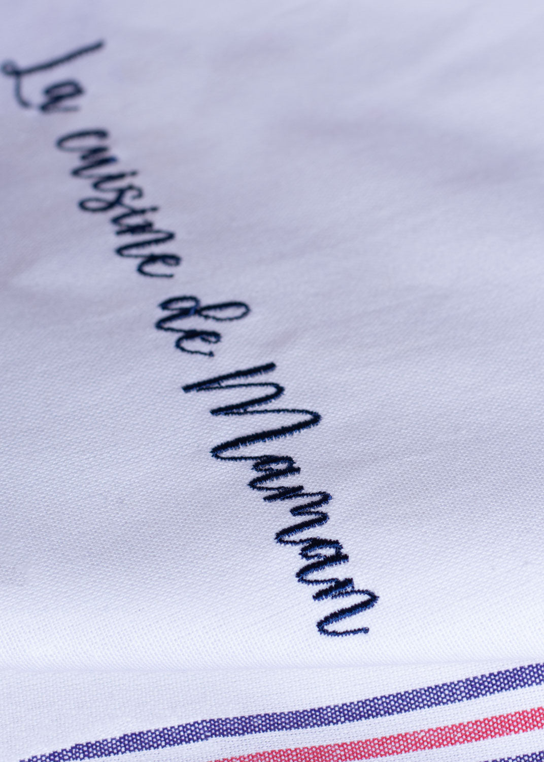 Gros plan d'une broderie personnalisée sur un torchon de cuisine en coton, confection française, avec l'inscription « La cuisine de Maman ».