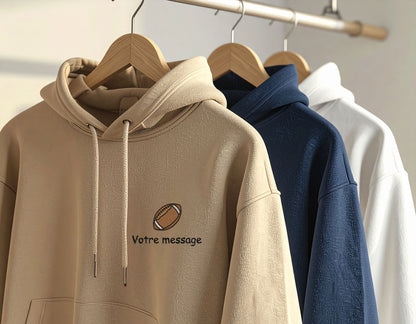 Sweat à capuche couleur sable avec broderie personnalisée football et texte "Votre message", présenté sur cintre aux côtés de sweats bleu marine et blanc.