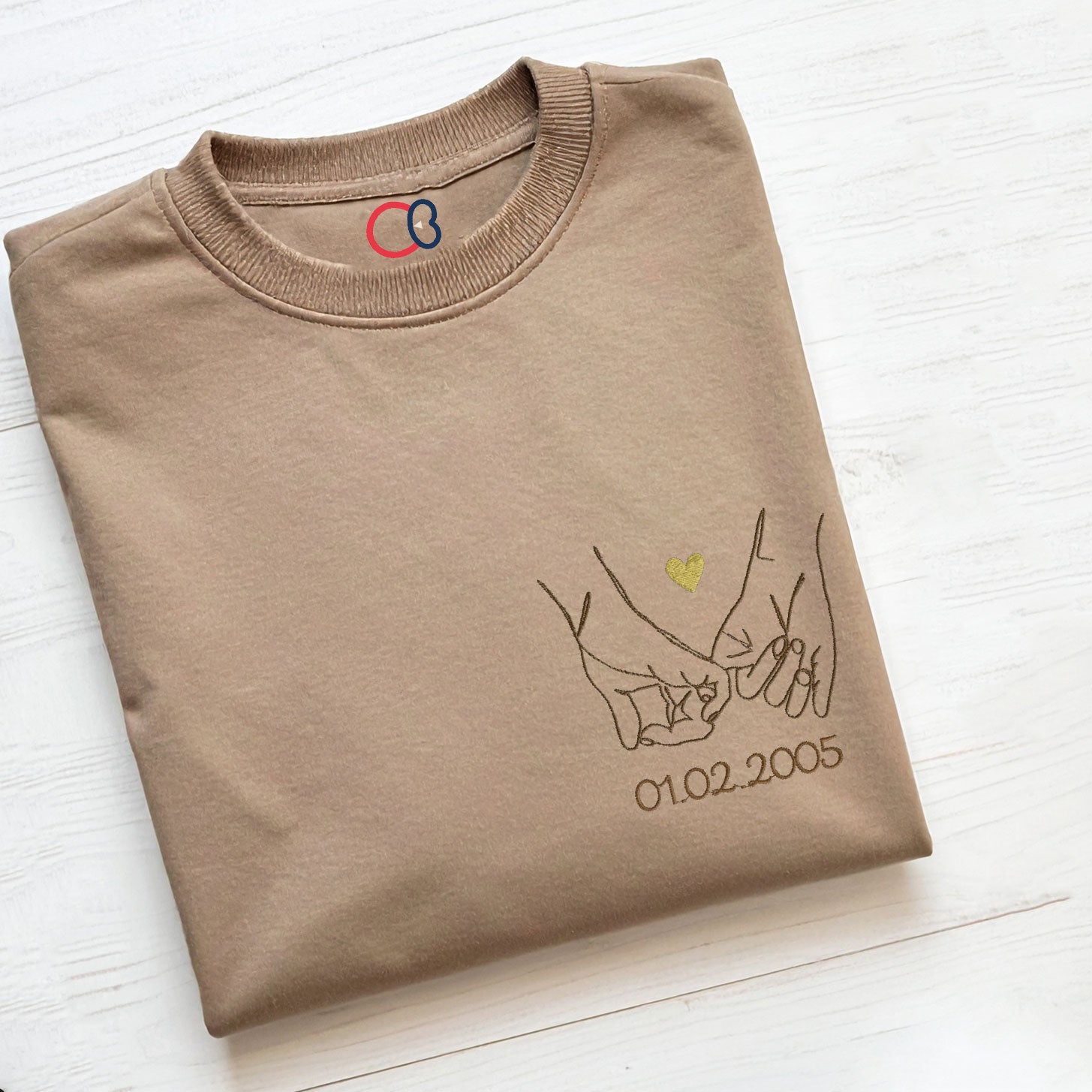 T-shirt beige brodé avec motif de mains entrelacées en line art, petit cœur doré et date personnalisée, idée cadeau Saint-Valentin ou anniversaire de couple.