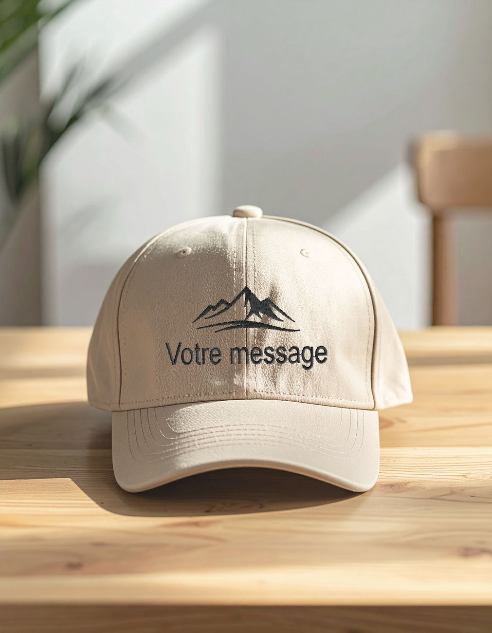 Casquette beige personnalisée en coton brossé, posée de face sur une table en bois clair avec broderie message et motif montagne.