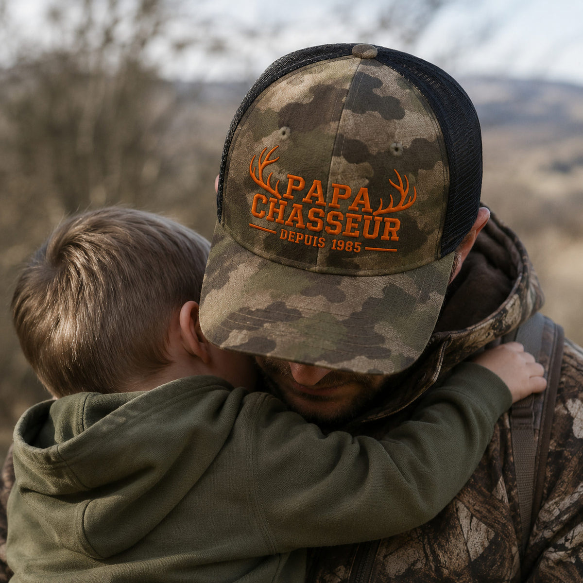 Père portant une casquette camouflage brodée Papa Chasseur avec son enfant dans les bras