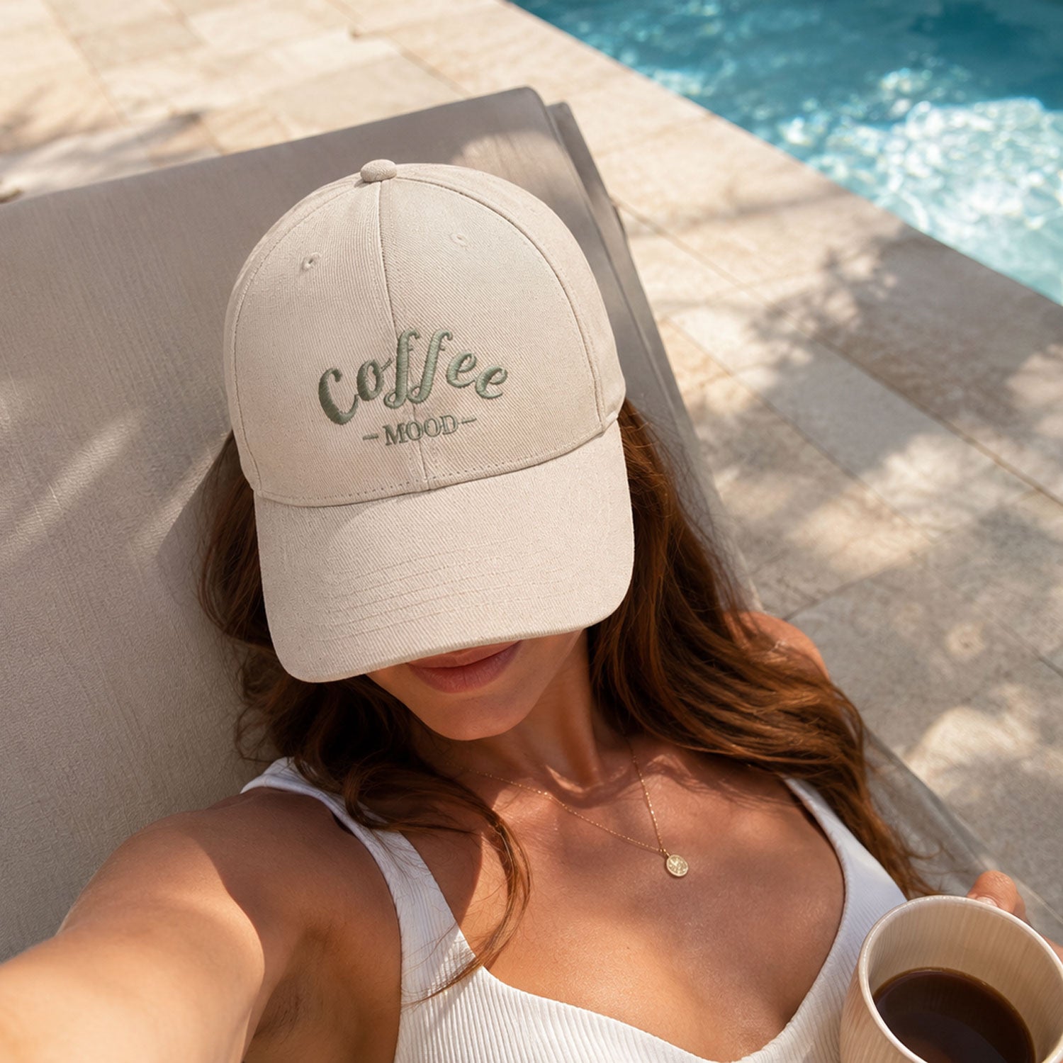 Femme au bord d'une piscine portant une casquette personnalisée brodée Coffee Mood de la Collection Signature. Casquette en coton couleur crème, idée cadeau personnalisée fabriquée en France.