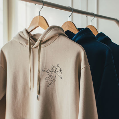 Sweats a capuche brodes avec un cupidon et un coeur en couleurs sable et bleu petrole presentes sur cintres
