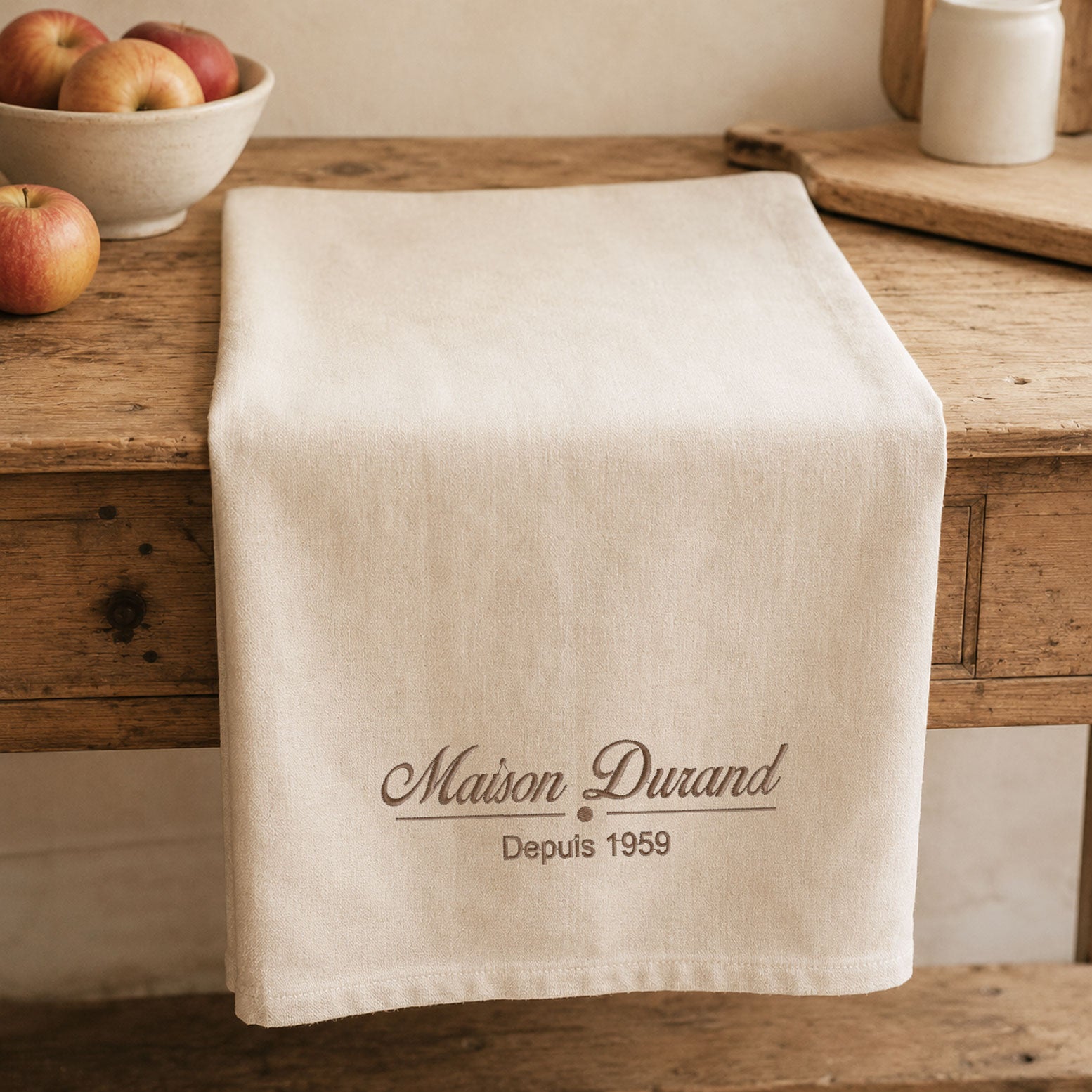 Torchon de cuisine personnalisé brodé Made in France avec le nom de famille Maison Durand, présenté sur une table en bois dans une cuisine de style campagne chic. Cadeau personnalisé pour la cuisine.